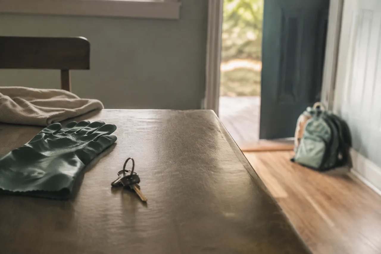 Luvas de trabalho, chaves e mochila infantil diante de uma porta aberta